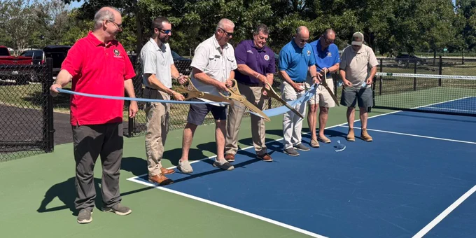 group of people cutting a ribbon at the new pickleball courts
