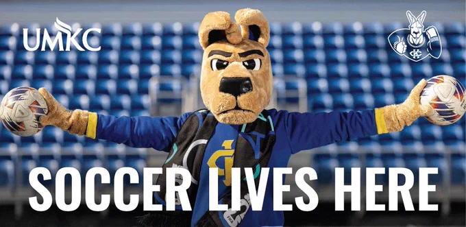KC Roo mascot poses in Durwood Stadium, holding a soccer ball in each paw with arms stretched out.