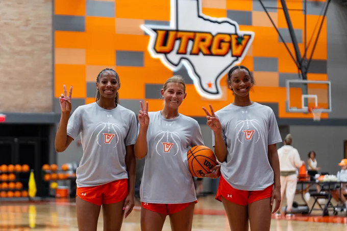 Three UTRGV women's basketball players posing together on an indoor court, smiling at the camera and holding up peace signs.
