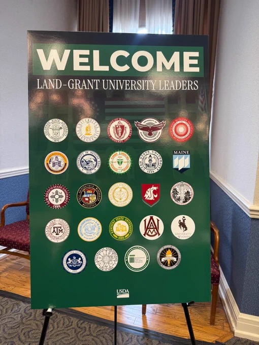 A display board with the heading "Welcome Land-Grant University Leaders" features various university logos, including Texas A&M University, University of Missouri, Washington State University, and University of Maine. The USDA logo is at the bottom.