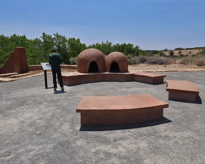 A person reading an informational sign near two traditional adobe hornos at the San Antonio Oxbow Bluffs Open Space.