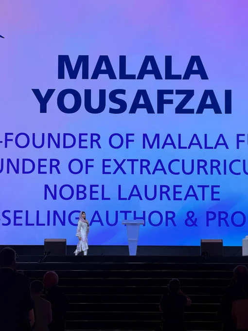 Nobel Peace Prize laureate Malala Yousafzai walks across the stage during a Rotary International Convention general session in Taipei. A large screen behind her displays her name and highlights her roles as co-founder of Malala Fund, Nobel laureate, and bestselling author as attendees look on.
