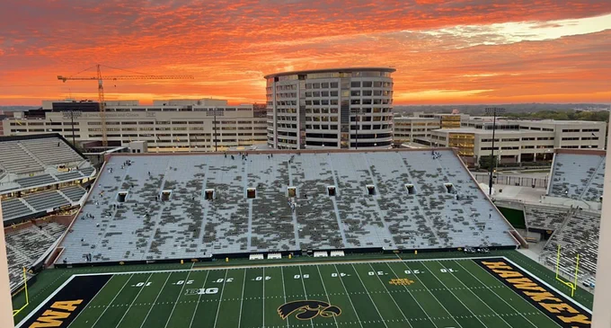 A panoramic view of Kinnick stadium at sunrise with vibrant orange and pink sky with clouds overhead featuring the University of Iowa Children's Hospital