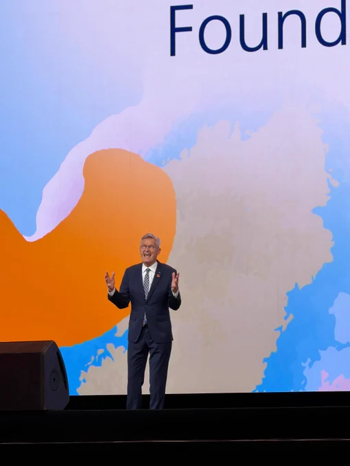 Holger Knaack speaks from the main stage during a Rotary International Convention general session in Taipei. He gestures with both hands while presenting in front of a colorful Rotary Foundation backdrop.