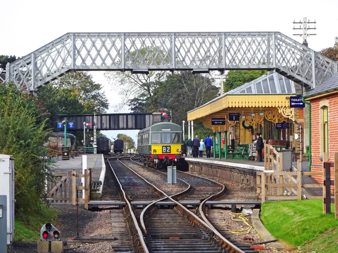 Viewed from the level crossing separating the North Norfolk Railway from the National Rail network, a BR green Class 101 DMU stands at the former Cromer-bound platform with its ornate and beautifully restored canopy.