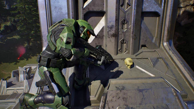Master Chief crouches on a structure, aiming a weapon with concentrated focus. In the foreground, a skull rests on the surface.