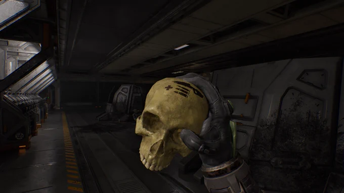 A hand in a futuristic glove holds a yellow skull with markings resembling a gaming controller. The background features a dark, metallic spaceship interior with dim lighting and various structures.