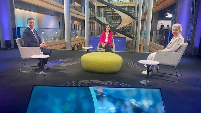 Drei Personen sitzen in einem Fernsehstudio an einem runden Tisch.