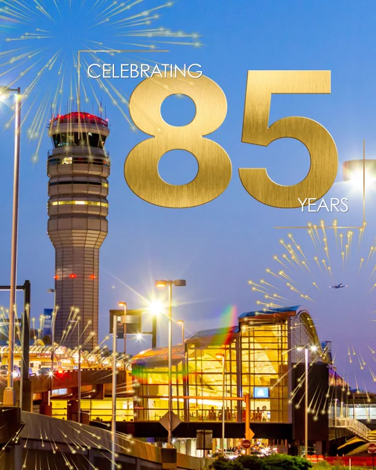 A nighttime view of an airport with a control tower and modern Reagan National Airport. Large, golden text reading "Celebrating 85 Years" is prominently displayed against a background of fireworks in the sky.