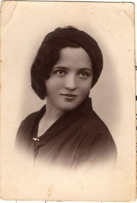 Vintage black and white portrait of a woman wearing a beret and a dark coat with a pin, looking directly at the camera.
