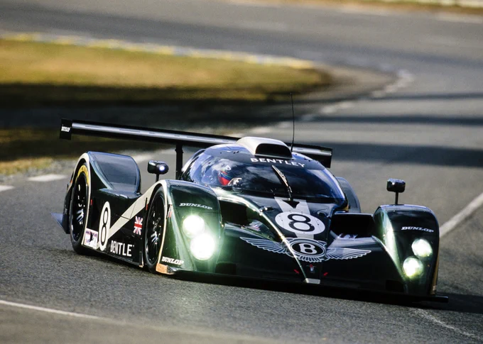 A low sun casting long shadows across the track behind, the British racing green Bentley EXP Speed 8 steers around a left hand corner, headlights glowing. 2001 Le Mans 24 Hours, LAT Images