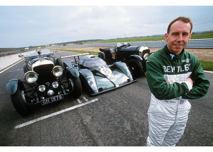 On the right of frame, Andy Wallace stands on the track with his arms folded wearing a green and white Bentley race suit, looking at the camera. Behind, his modern Bentley EXP Speed 8 is parked between two vintage Bentleys, with a 1930 Speed Six on the left. Bentley Le Mans Test, Snetterton, April 2001, Clive Rose/LAT Images