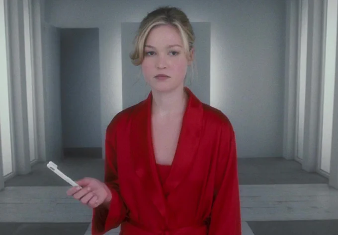Julia Stiles in red robe holding a toothbrush.