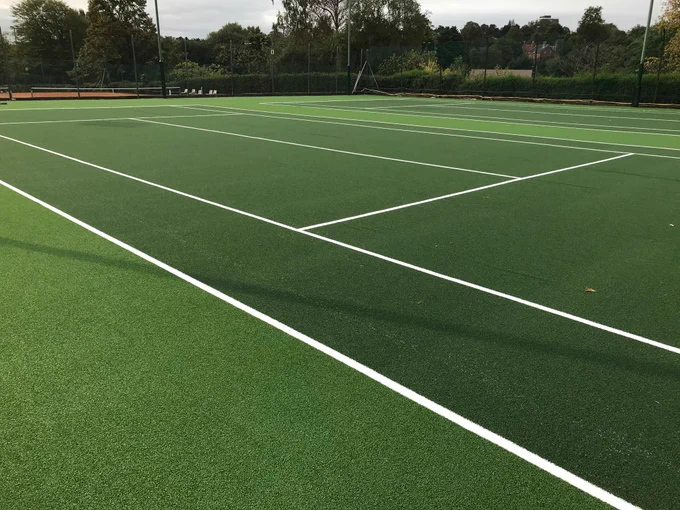Empty outdoor tennis court with freshly painted white lines surrounded by trees under a cloudy sky.