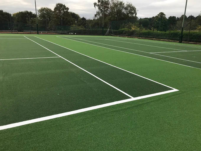 Empty outdoor tennis courts with freshly painted white lines under a cloudy sky and surrounded by trees.