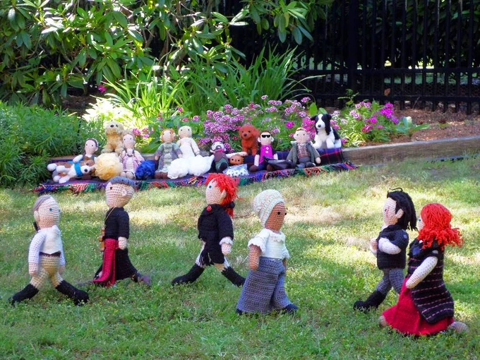 Crochet dolls of Benjamin Tallmadge & Abigail on defense as Don Bruciare Gormangia, John Graves Simcoe and Ross & Demelza Poldark advance down the pitch.  More crochet fans, toy dogs & garden in backgroun. 