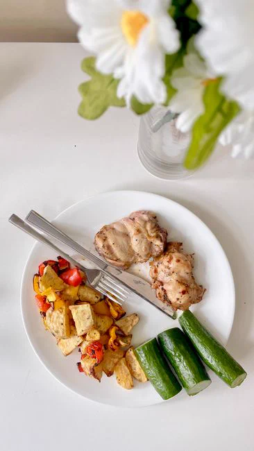 Top view of a nutritious meal featuring grilled chicken, vegetables, and fresh cucumbers on a white plate.