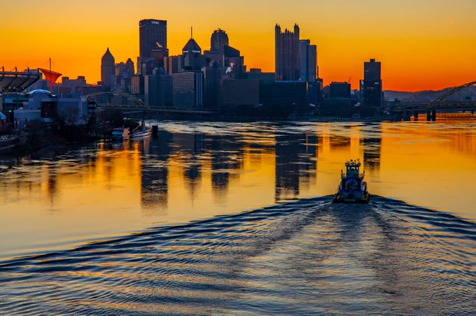 A towboat navigates the Ohio River at sunrise as the city is seen in the background