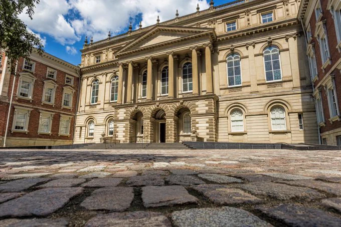 Grand neoclassical building with tall columns and arched doorways under a partly cloudy sky.