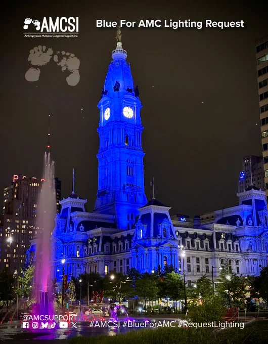Philadelphia City Hall is illuminated in blue at night, highlighting the historic clock tower and architectural details in support of AMC Awareness Day. The AMCSI logo appears in the upper-left corner, with the AMC footprint symbol in the upper-right corner.