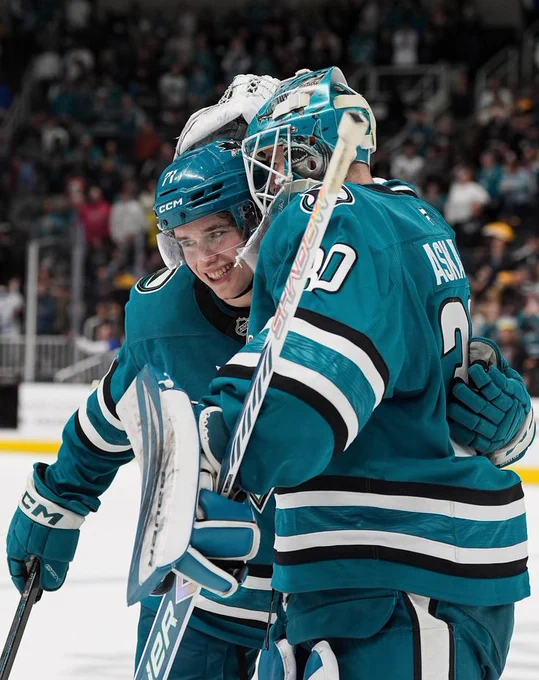 Yaroslav Askarov hugging Macklin Celebrini on the ice in the Sharks' teal jersey