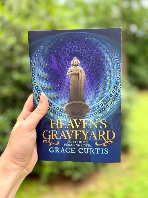 hand holding up a book in front of a blurry landscape