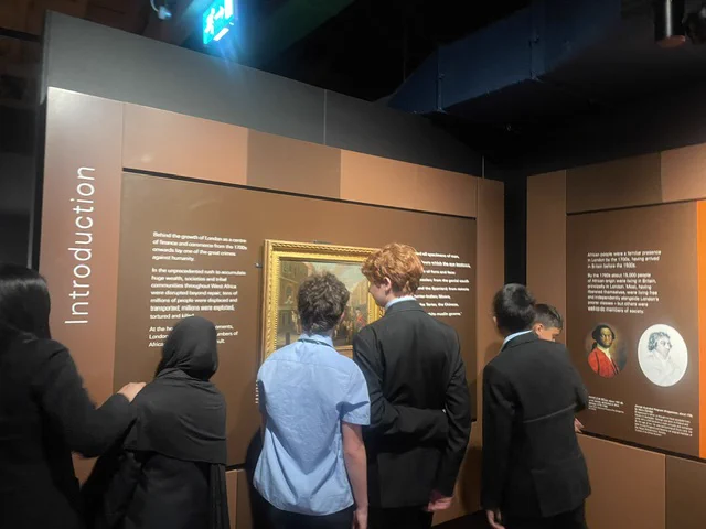 A group of students examining artwork in a museum exhibition. The setting is designed to be educational and informative.