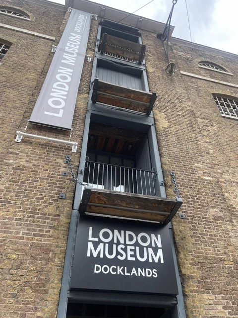 View of the London Museum Docklands building facade showcasing its industrial architecture. A vertical banner and sign are visible.