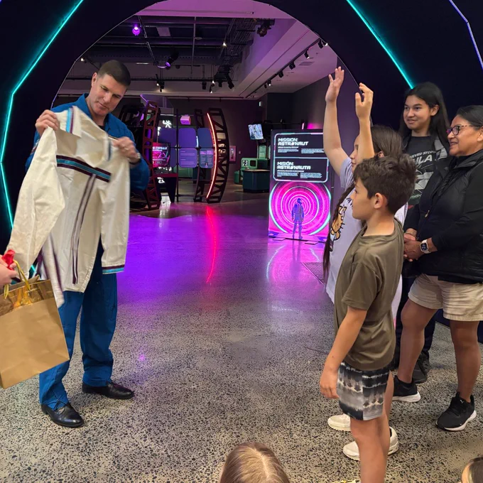 An astronaut showing a garment to a group of children in a museum.