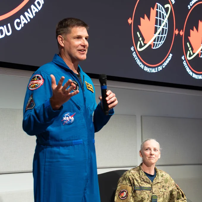 An astronaut in a blue flight suit speaking at a presentation.