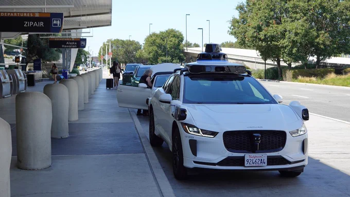 A Waymo vehicle sits at the curb outside Terminal B Departures.