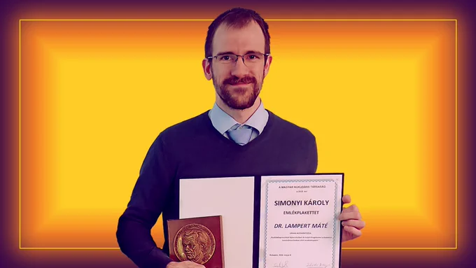 Máté Lampert, a staff research physicist at PPPL, holds the Károly Simonyi Memorial Plaque from the Hungarian Nuclear Society. Background is yellow, orange and red.