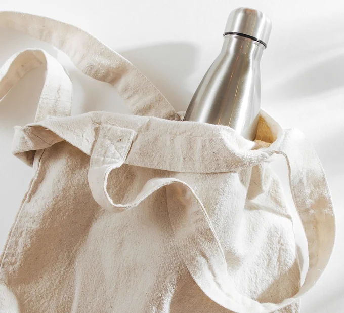 Reusable stainless steel water bottle in a recycled canvas tote bag.