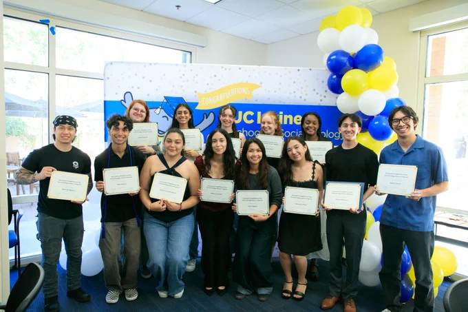 University of California, Irvine undergraduate students hold certificates in front of a decorated backdrop with blue, yellow, and white balloons at theSchool of Social Ecology's  2026 Honors & Awards celebration. Photo by Han Parker