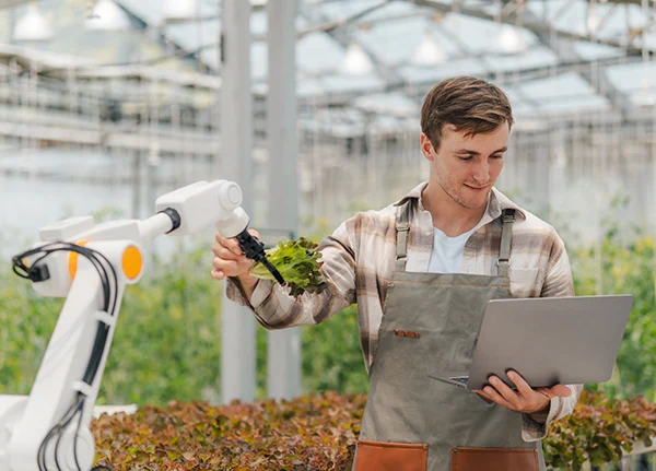 A young Caucasian man using a laptop computer while working in a greenhouse.