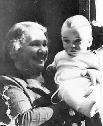 Historical black and white photo showing a woman holding a young child. A woman is smiling broadly.
