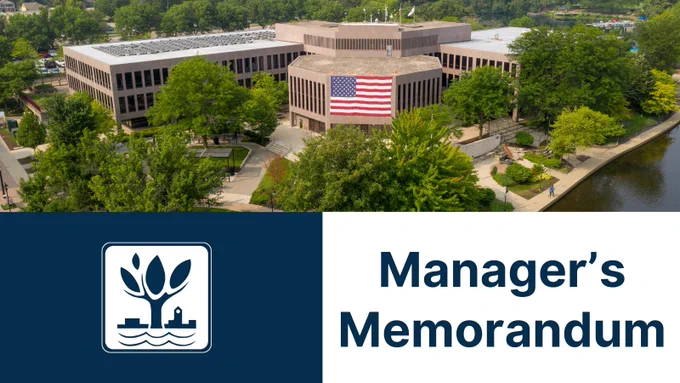 A horizontal graphic for the City of Naperville. The top half features a wide, aerial photograph of the Naperville Municipal Center, a multi-story concrete building with an American flag displayed on the front, surrounded by green trees and the riverwalk. The bottom half is split: a dark blue block on the left contains the white City of Naperville logo, and a white block on the right features the words "Manager’s Memorandum" in large, dark blue serif font.