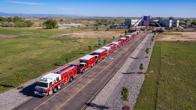 Fire apparatus parked along a long drive with the American flag hanging in the distance