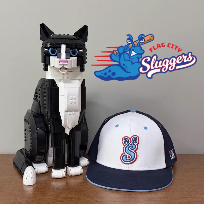 A navy blue and white Flag City Sluggers baseball cap with HATS the Lego Cat and a Flag City Sluggers logo in the upper right-hand corner of the photo