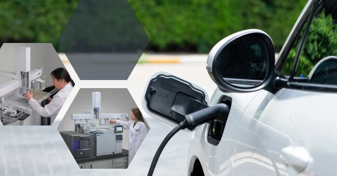 White electric car plugged into a charging station outdoors with green bushes in the background.