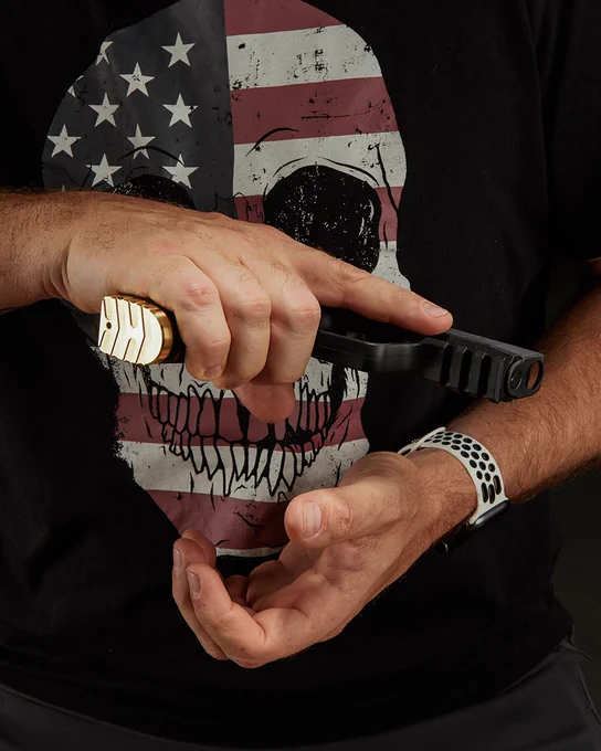 Shooter holding a SIG P365 X Macro pistol equipped with a brass magazine base plate, demonstrating the installed upgrade in use.