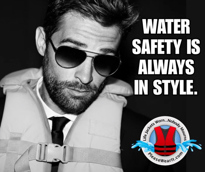 Black-and-white graphic showing a man wearing sunglasses and a life jacket over a dress shirt and tie while holding a drink. Bold white text reads, \u201CWATER SAFETY IS ALWAYS IN STYLE.\u201D A circular water safety logo in the corner includes a red life jacket and the phrases \u201CPlease Wear It\u201D and \u201CHave Fun \u2013 Nobody Drowns.\u201D