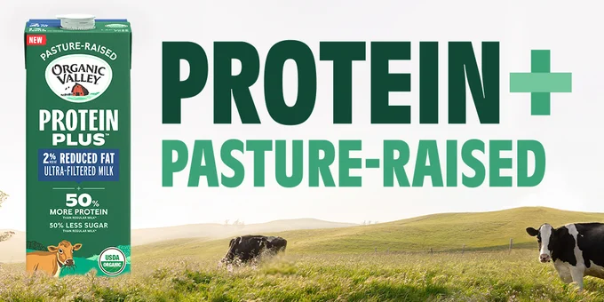 A carton of Organic Valley Protein Plus 2% reduced fat ultra-filtered milk is displayed with text highlighting "50% More Protein" and "50% Less Sugar." The background features a pastoral scene with cows grazing in a field with the text "Protein   Pasture-Raised."