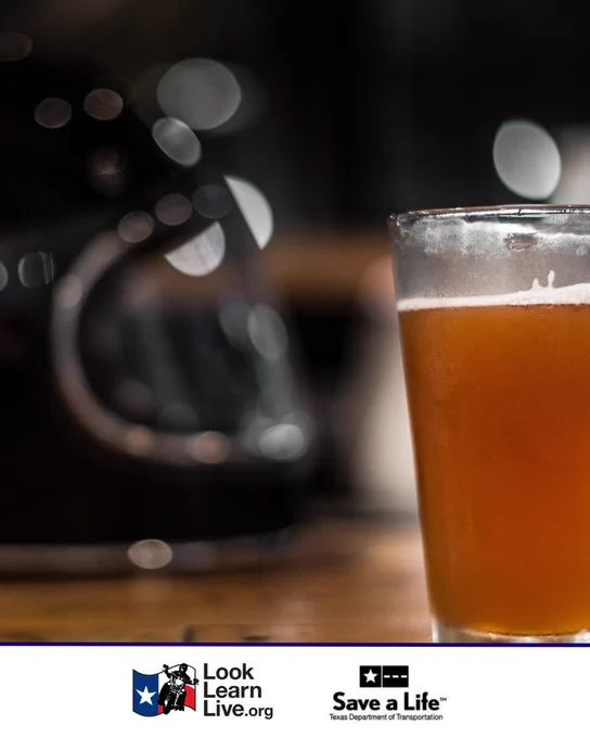 A glass of beer is placed on a wooden table. The background shows a blurred motorcycle helmet. Logos for Look Learn Live and Texas Department of Transportation's "Save a Life" are at the bottom.