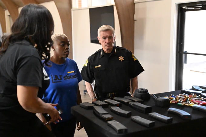 A group of individuals stands around a table displaying various firearm magazines and equipment.