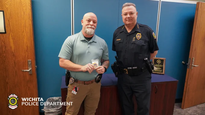 Two individuals stand in an office setting, one holding a badge. Both are wearing uniforms with Wichita Police Department insignia. A plaque is visible on a cabinet behind them, and the department logo is displayed in the image corner.
