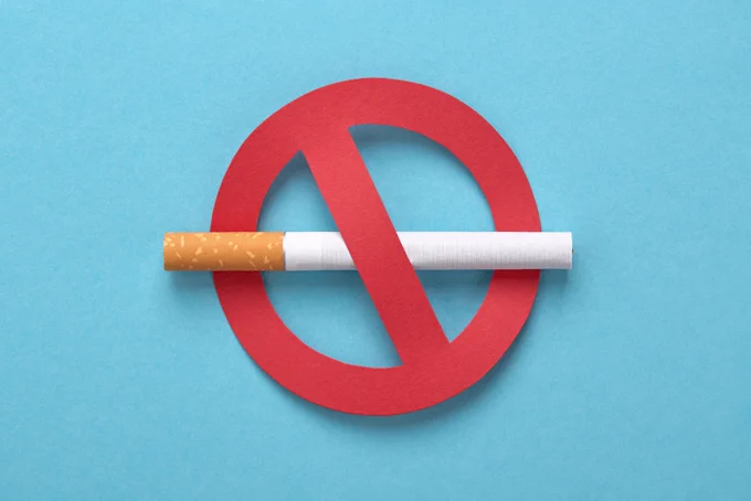 A cigarette is placed through the center of a red "no" symbol, indicating a no smoking sign, against a blue background.