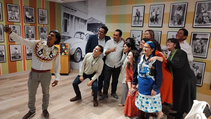 A group of participants smiling and posing for a selfie in a room decorated with black and white photos during the final day of the exchange. One person is in the front of the group holding a phone to take the picture. 