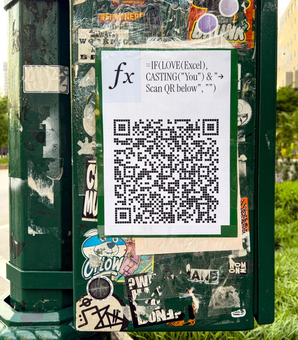 A sticker on a pole covered with various colorful stickers. The main sticker contains a formula using Excel syntax and a QR code for scanning. Text reads: 'fx =IF(LOVE(Excel), CASTING('You') & '>, Scan QR below', '')
