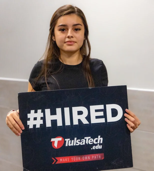Person holding a Tulsa Tech sign with #HIRED in bold letters, celebrating job placement success.